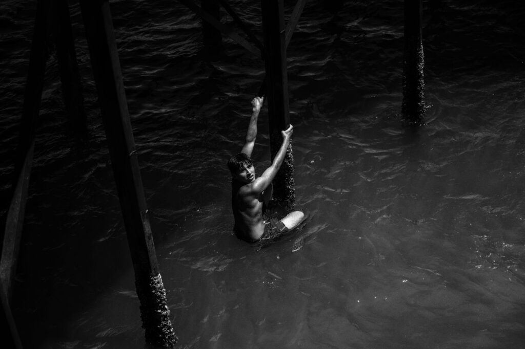 A man in Bahía de Kino climbs a pier. Black and white dramatic scene.