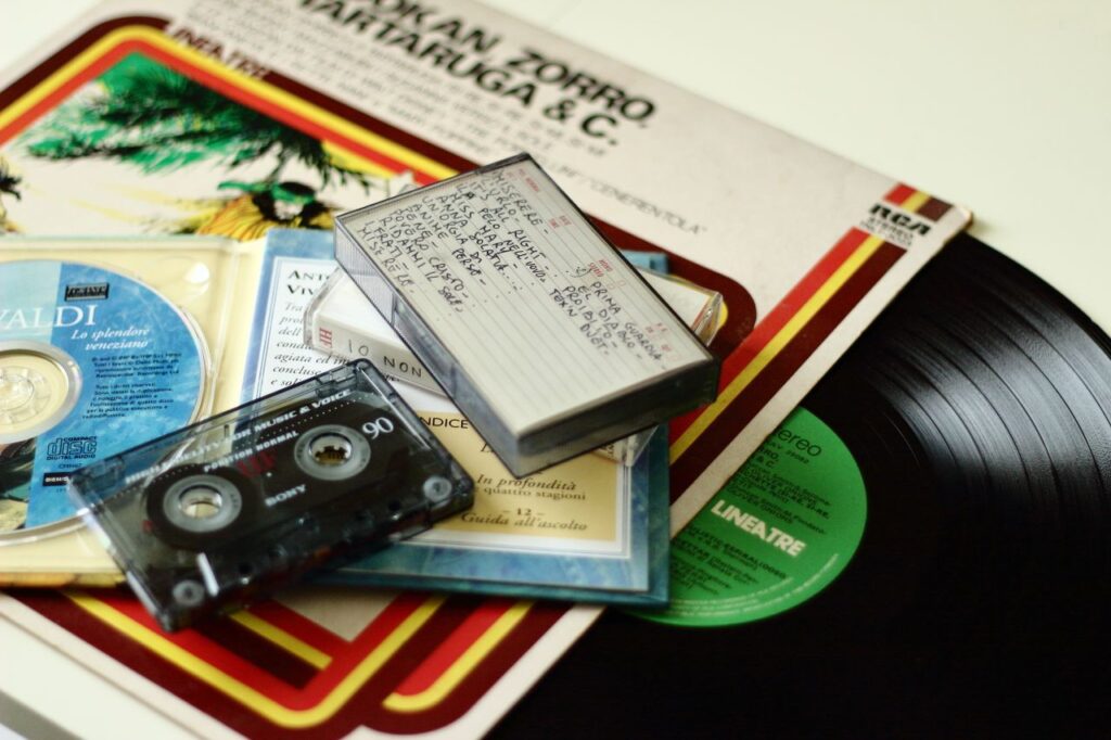 A nostalgic mix of old media formats including vinyl records, cassette tapes, and a compact disc.